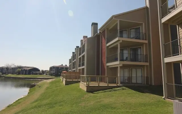 Apartment Complex by the Water View of an apartment complex next to a serene body of water with green grass in the foreground.