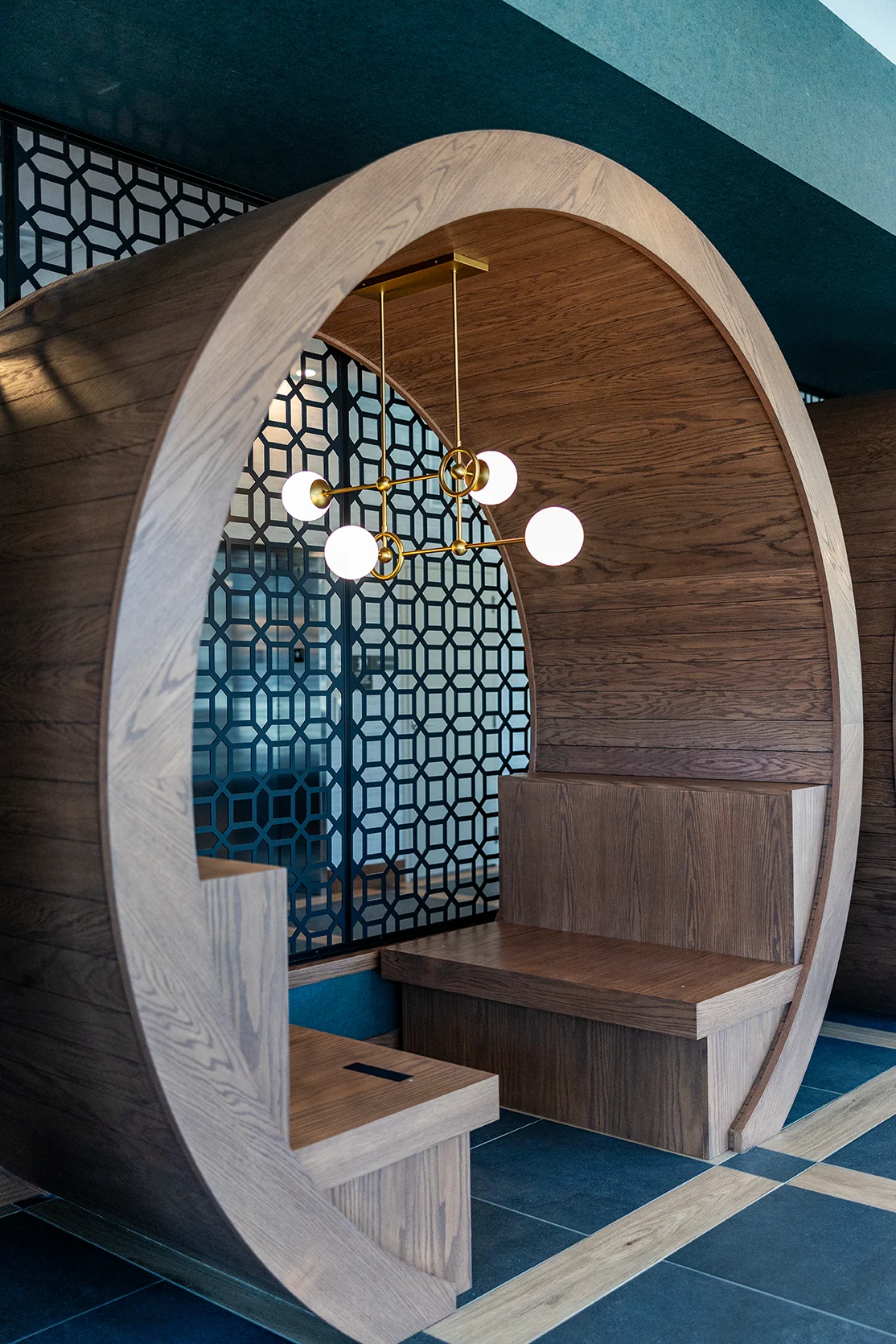 Modern Circular Seating Design A unique circular wooden seating area with a modern design, featuring a geometric patterned background and hanging light fixtures.