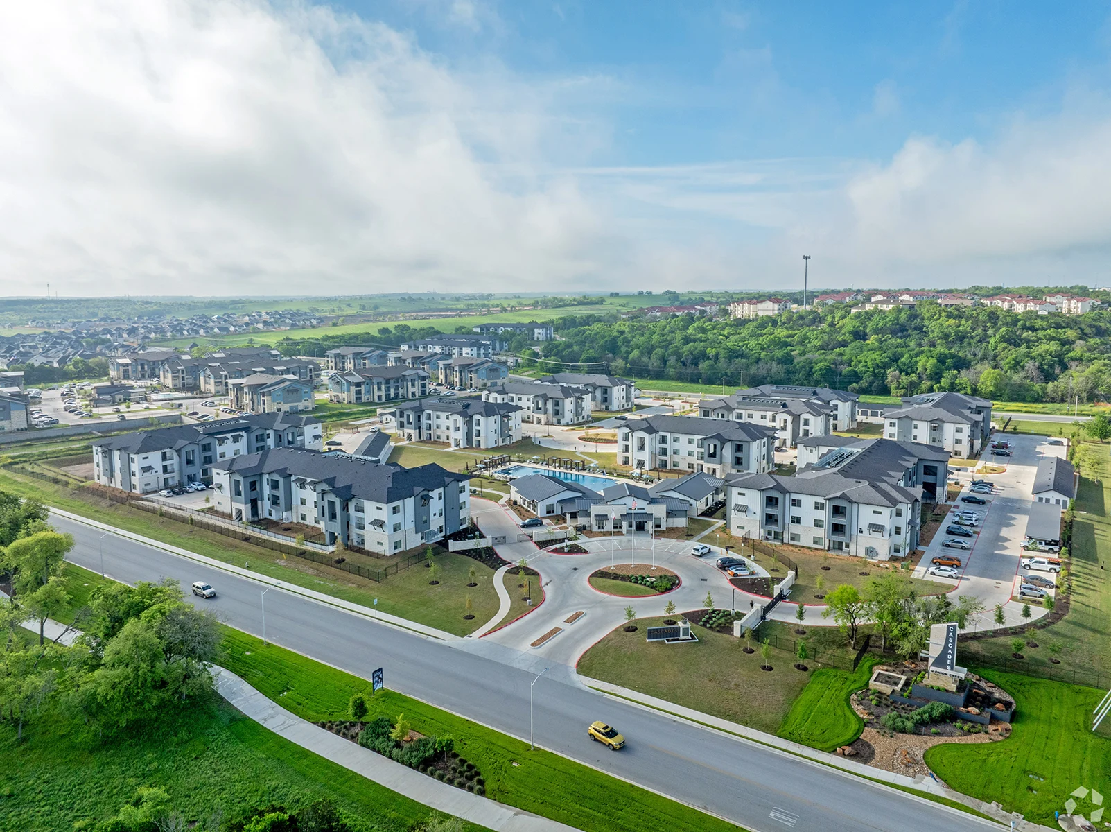 Aerial view of a modern apartment complex surrounded by greenery and a road.
