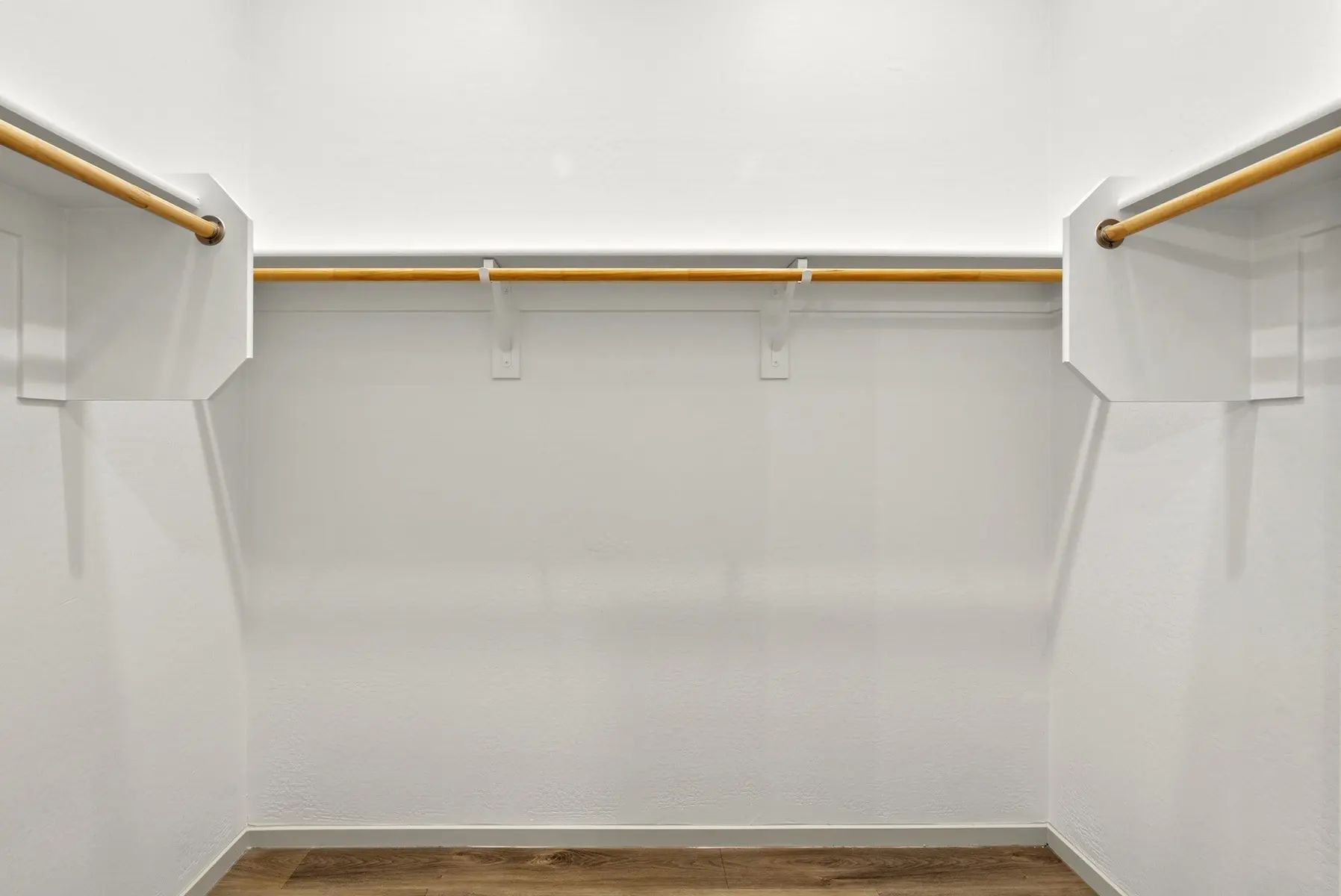Empty closet with two hanging rods on white walls and wooden flooring, showcasing a minimalist design.