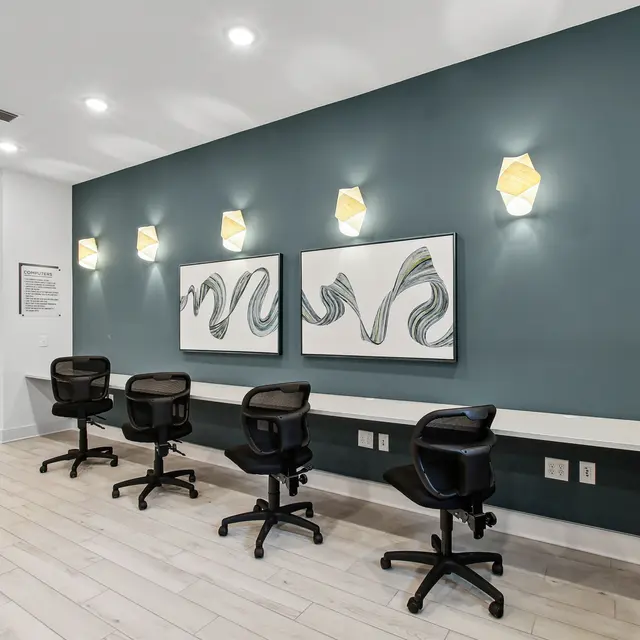 EKOS Lake Shadow A modern workspace featuring a dark blue wall with abstract art, stylish lighting, and several black office chairs around a white counter.