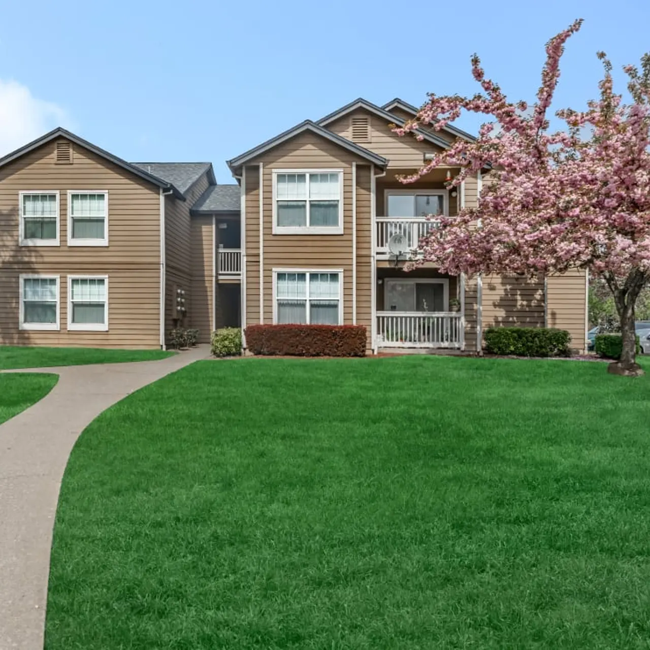 View of a two-story apartment building surrounded by green grass and a blooming cherry blossom tree.