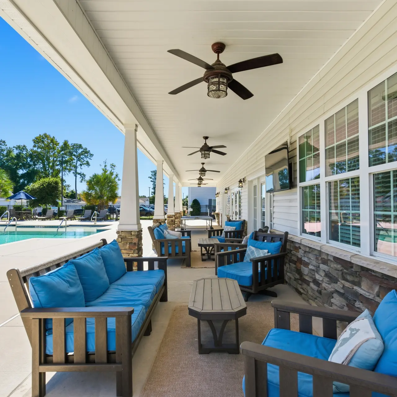 A spacious outdoor seating area featuring several wooden chairs and tables, accented with blue cushions, beside a swimming pool.