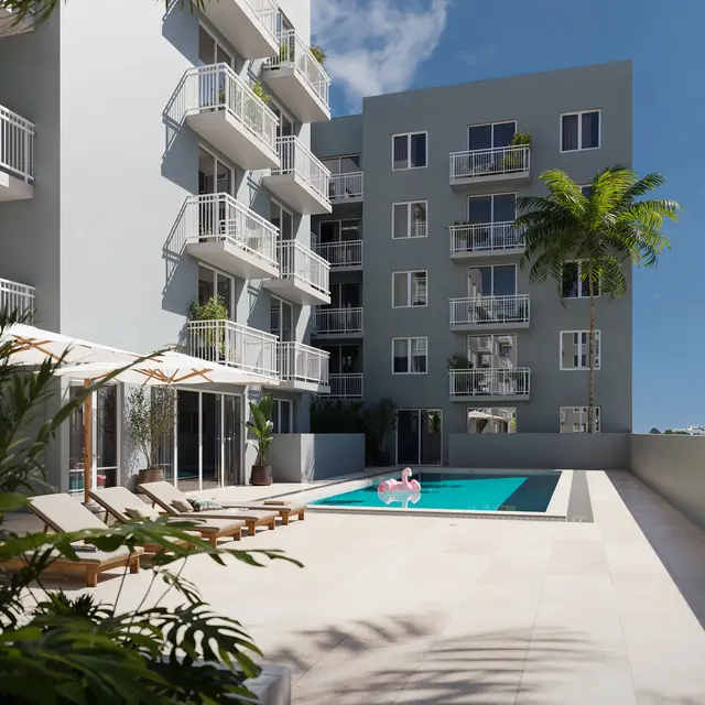 A modern apartment complex featuring a swimming pool and lounge chairs surrounded by tropical plants.