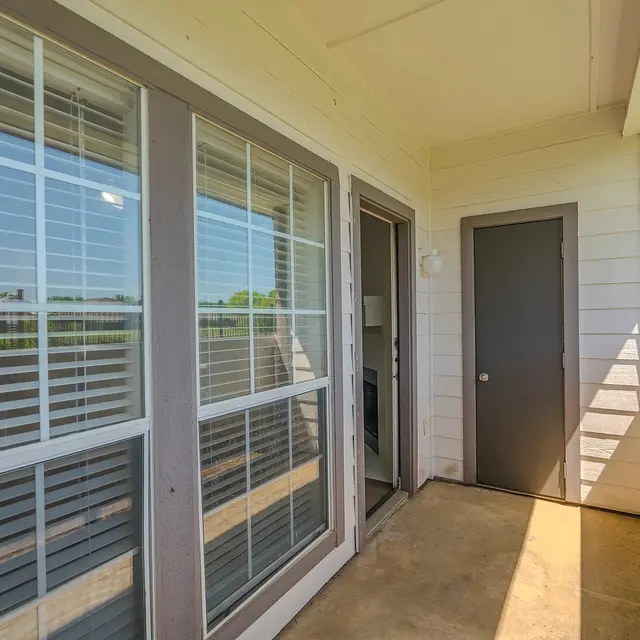 Exterior view of an apartment entrance with large windows and a door to the right.