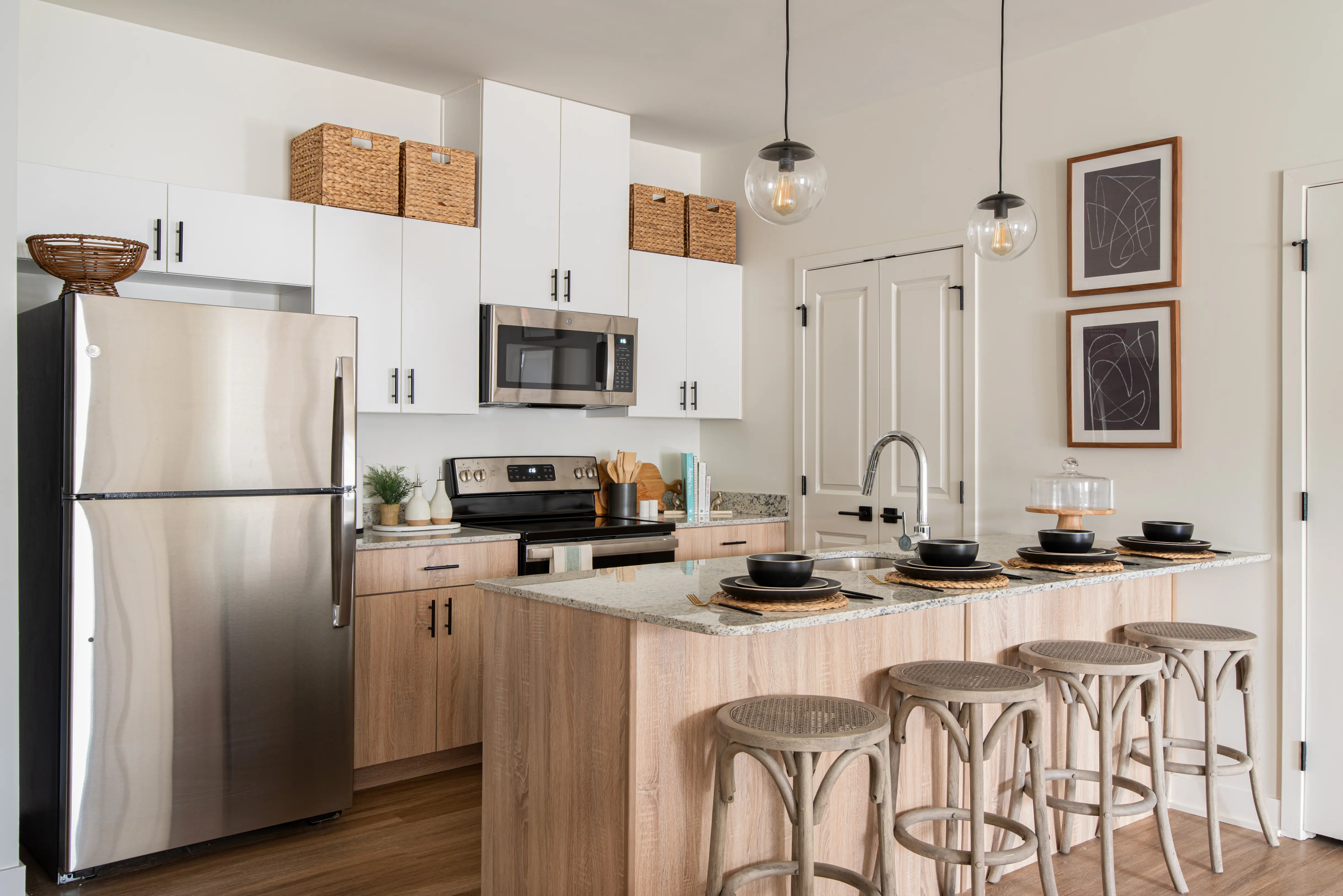 Modern Kitchen Design A modern kitchen featuring a stainless steel refrigerator, black stove, and countertop with bar stools, showcasing a blend of white cabinets and light wood elements.