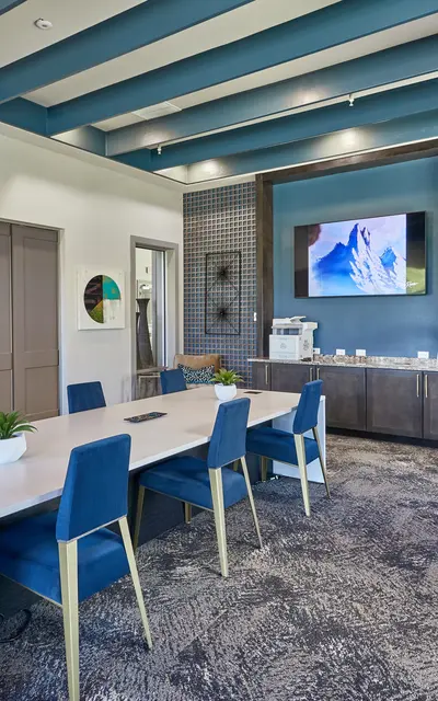 Modern conference room featuring a long table with blue chairs, a television mounted on the wall, and decorative elements.