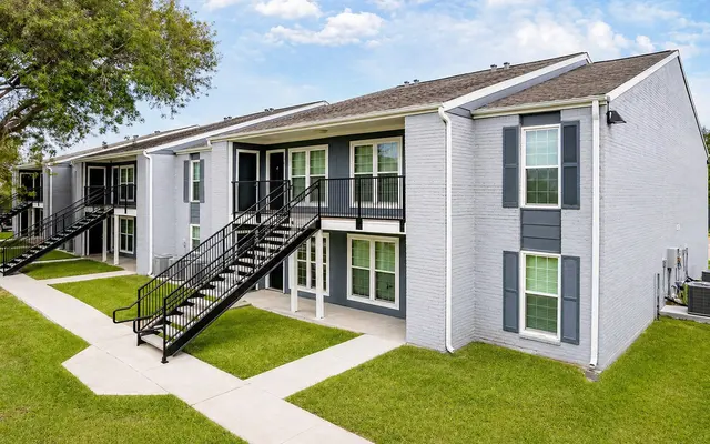 Exterior view of a modern apartment complex with two-story buildings, green lawns, and staircases leading to entrances.