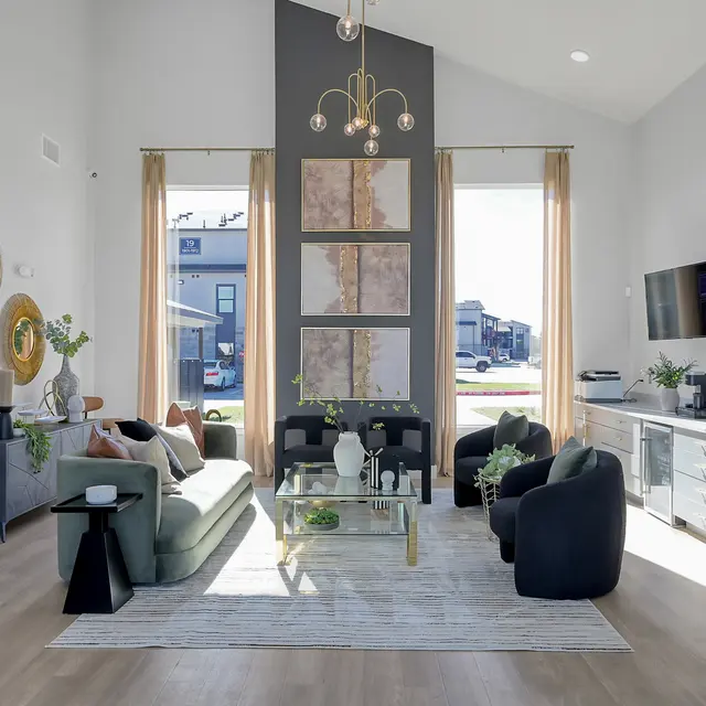 A modern living room featuring a large window, stylish seating, and decorative elements. The room has a neutral color palette with green accents, natural light, and contemporary decor.