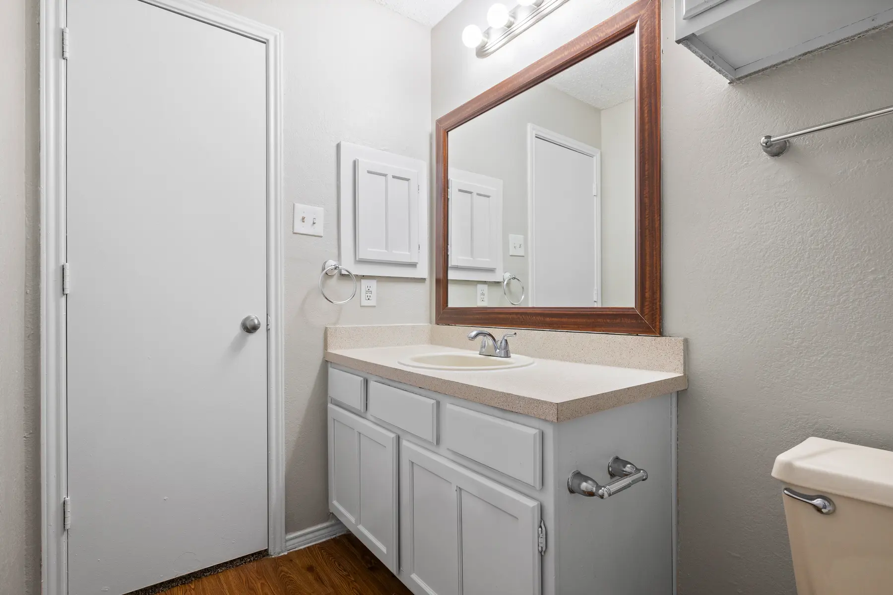 A clean and tidy bathroom featuring a mirror, sink, and wooden floor.