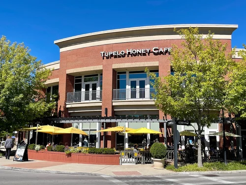 Exterior view of Tupelo Honey Cafe, featuring yellow umbrellas and brick architecture.