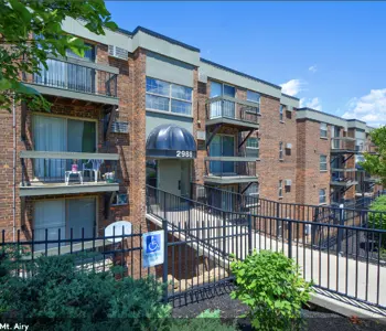 Exterior view of a multi-story brick apartment building with balconies and a sloped entrance ramp.