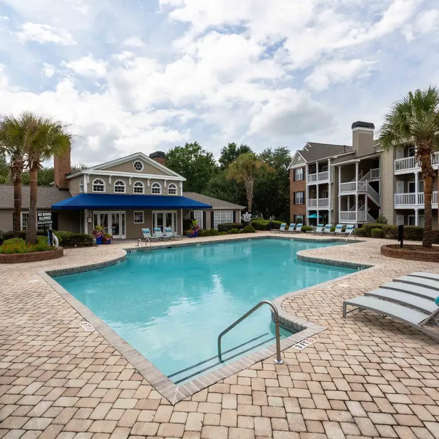 View of a swimming pool area in an apartment complex with chaise lounges and palm trees.