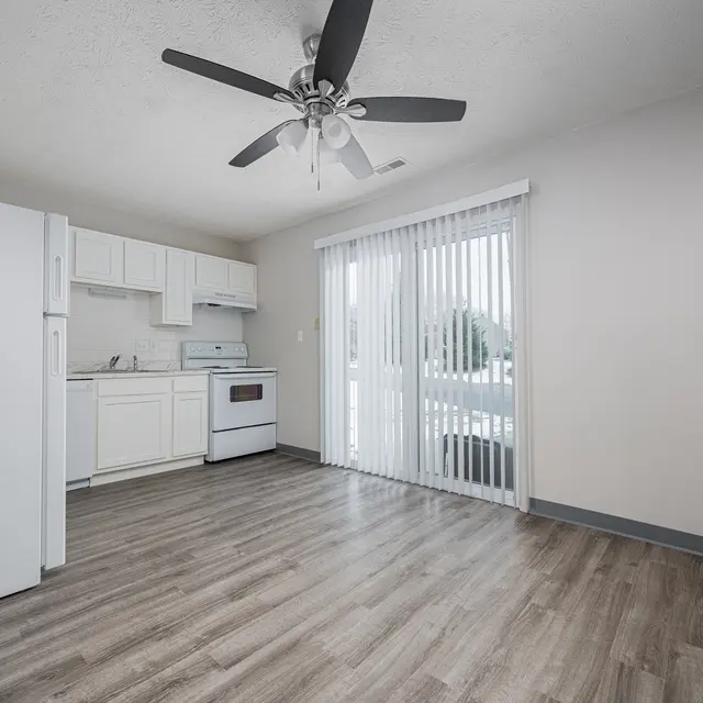 A modern kitchen with white cabinetry, an electric stove, a refrigerator, and a ceiling fan. Large sliding doors lead to the outside, with wood-like flooring throughout.
