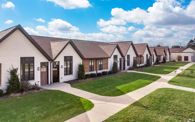 A row of modern townhouses with a green lawn and a paved pathway, under a partly cloudy sky.