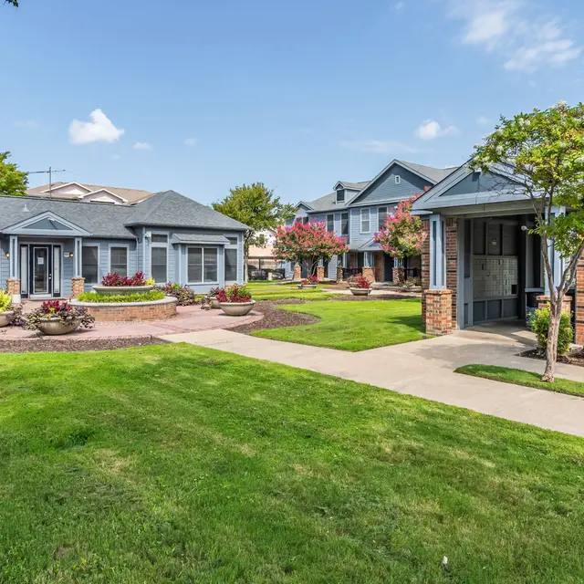 A well-maintained residential complex featuring green lawns, flower beds, and walkways connecting various buildings.