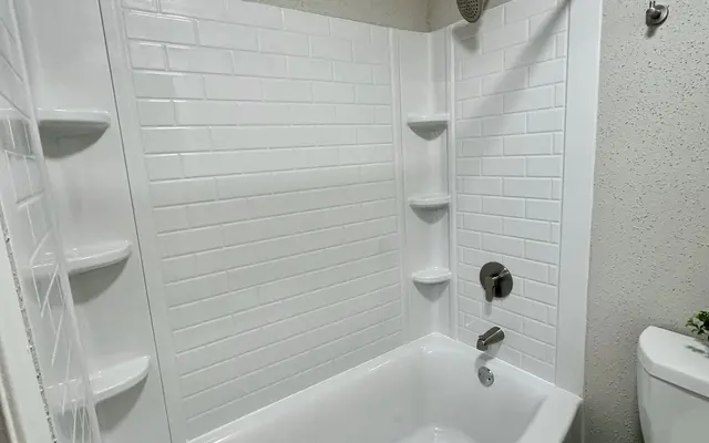 Modern Bathroom Design A modern bathroom with a white bathtub, tiled shower walls, and a toilet. The bathtub has a curved shape and the shower area features built-in shelves.