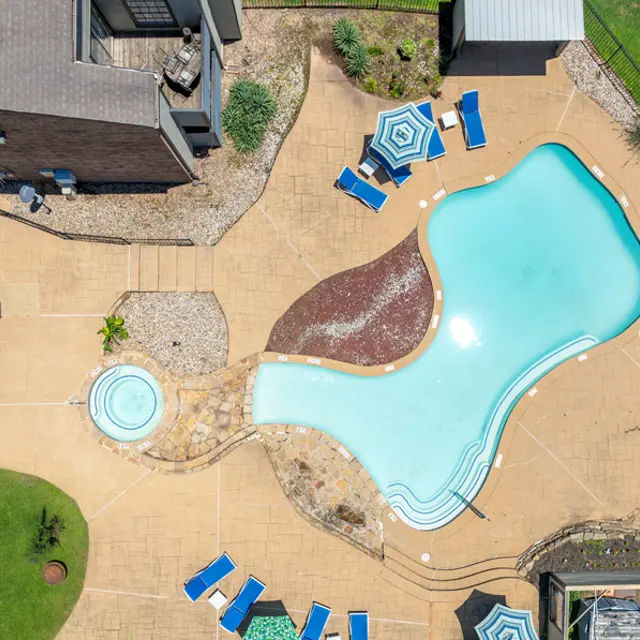 Aerial view of a shaped swimming pool surrounded by lounge chairs and umbrellas.