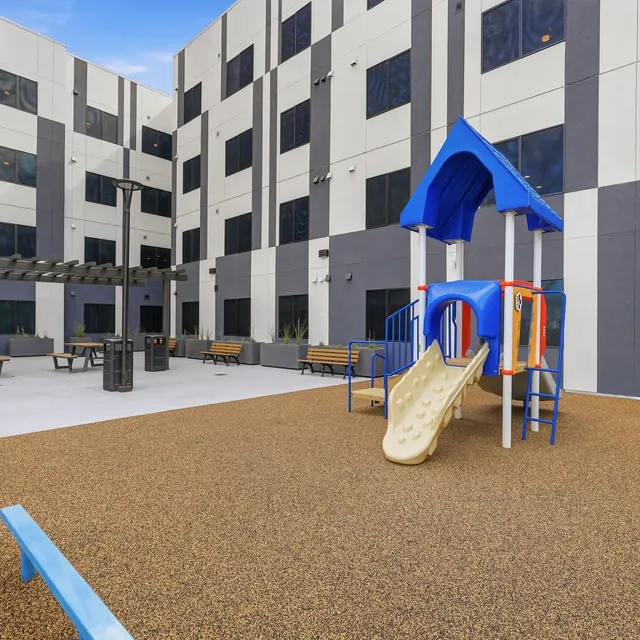 Modern Playground Area A playground area with a blue slide and colorful play structure, surrounded by seating and a modern building in the background.