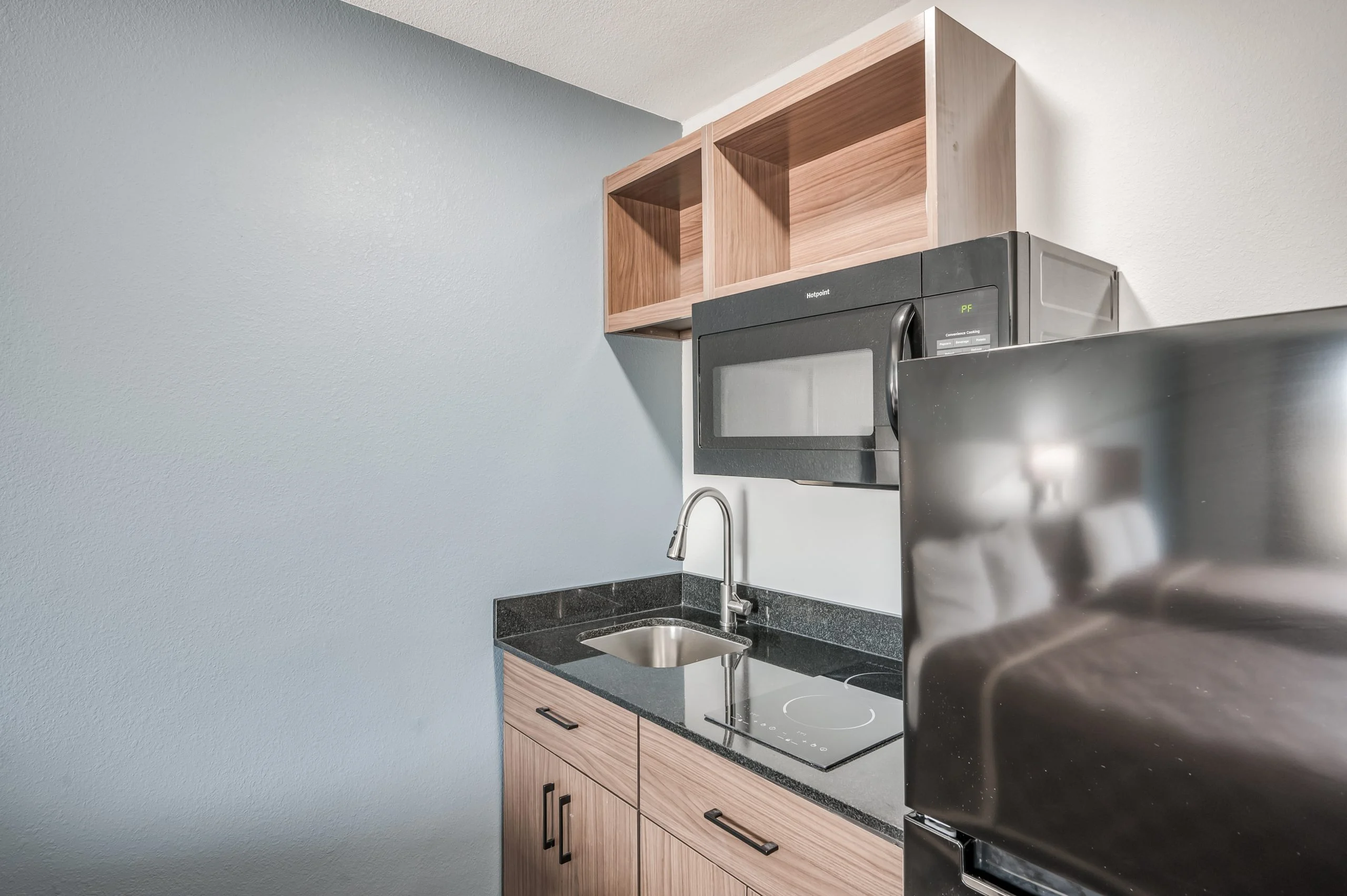 Modern Kitchenette A modern kitchenette featuring dark countertops, a sink, a microwave, and wooden cabinets above.