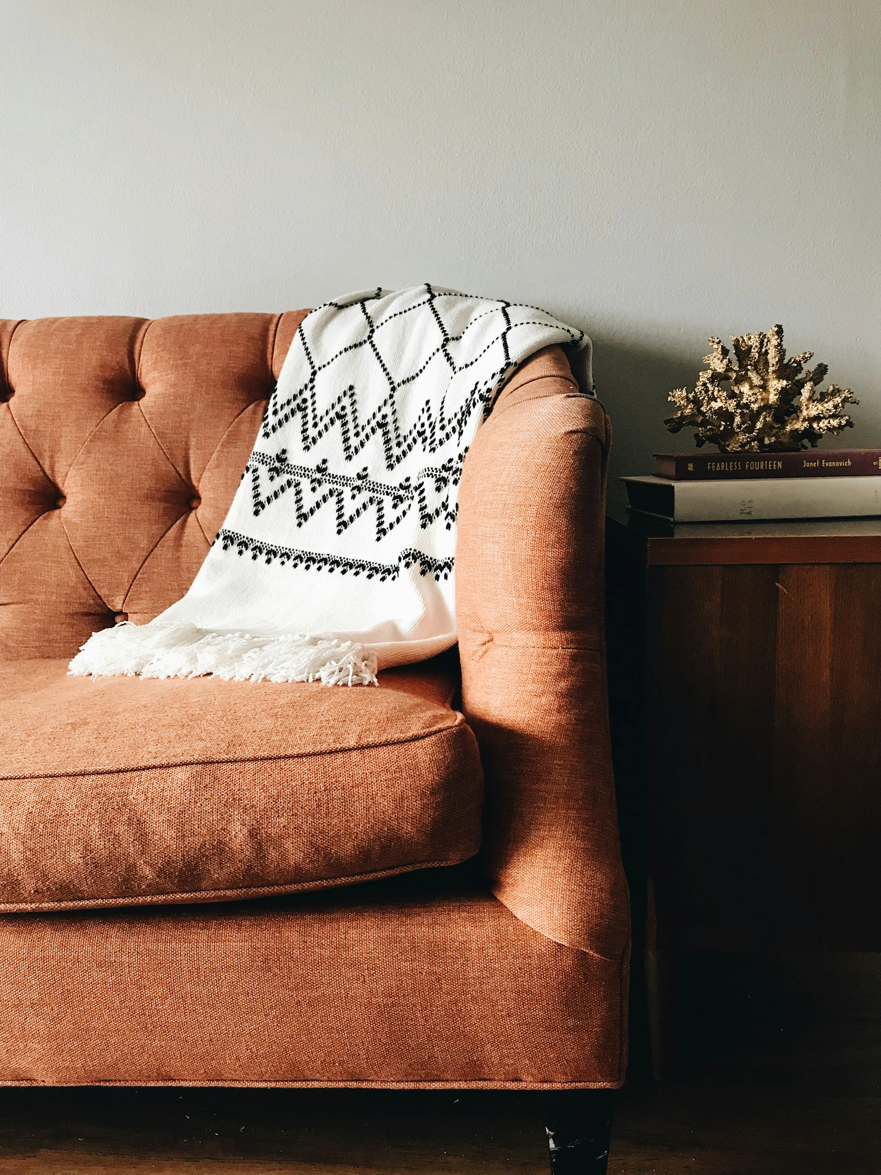A cozy brown sofa with a patterned black and white throw blanket draped over its arm, next to a wooden side table with books and decor.