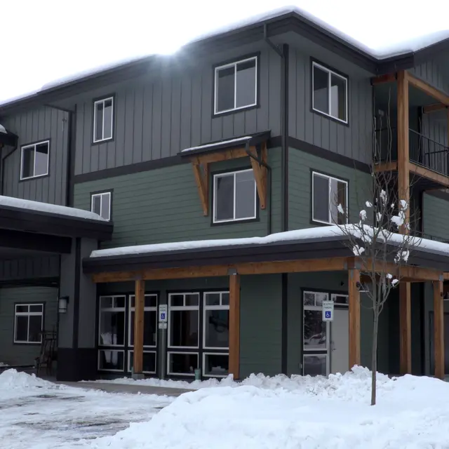 A modern three-story building covered in snow with large windows and wooden accents.
