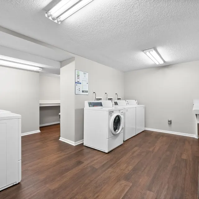A clean and well-lit laundry room featuring several white washing machines and a countertop area on the side.