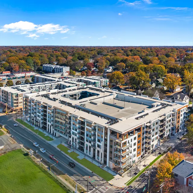 Aerial view of a modern apartment complex surrounded by autumn trees and urban landscape.