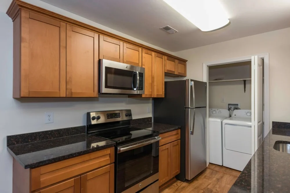 Modern Apartment Kitchen A modern kitchen featuring wooden cabinetry, stainless steel appliances, and a laundry area visible in the adjoining room.