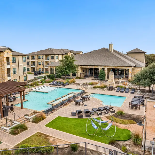 Aerial view of a residential complex featuring swimming pools, lounge chairs, and a clubhouse surrounded by greenery.