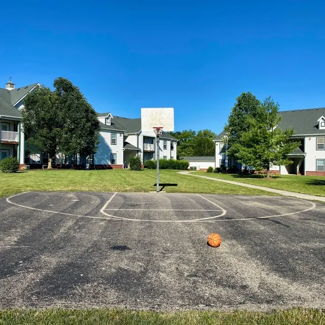 An outdoor basketball court surrounded by grassy areas and apartment buildings.