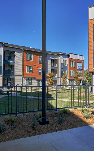 A modern apartment complex showcasing colorful buildings, with a fenced green area in the foreground and a clear blue sky above.