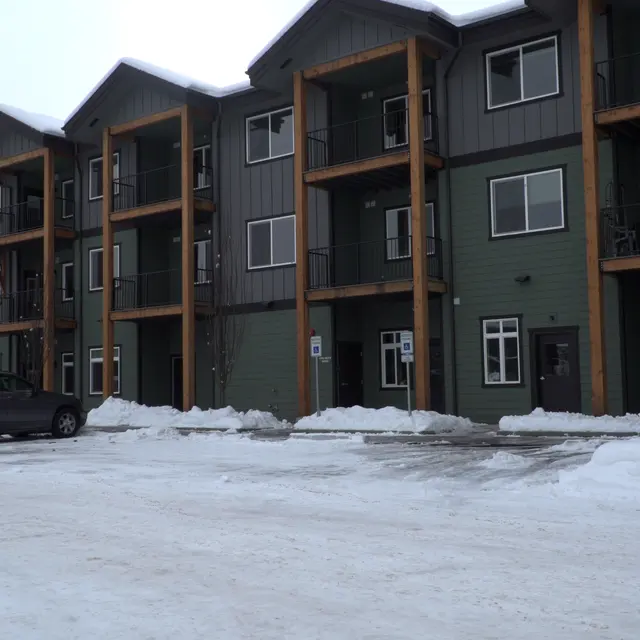 Modern Apartment Building in Snowy Landscape A modern apartment building with multiple stories and balconies, situated in a snowy environment.