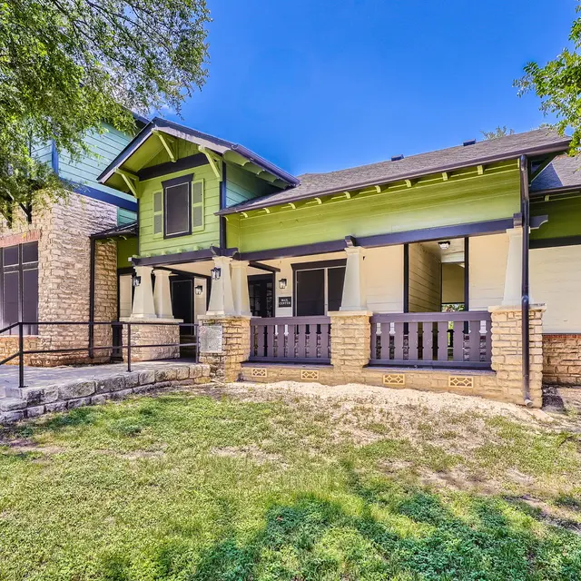 A charming house with a green exterior and stone accents, featuring a porch and a well-maintained lawn.