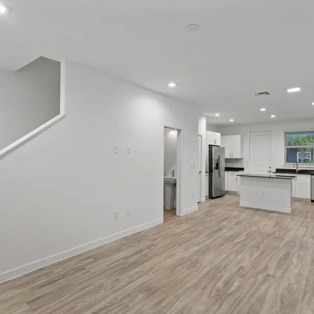 Bright and spacious modern kitchen and living area with wood flooring and a staircase leading to an upper level.