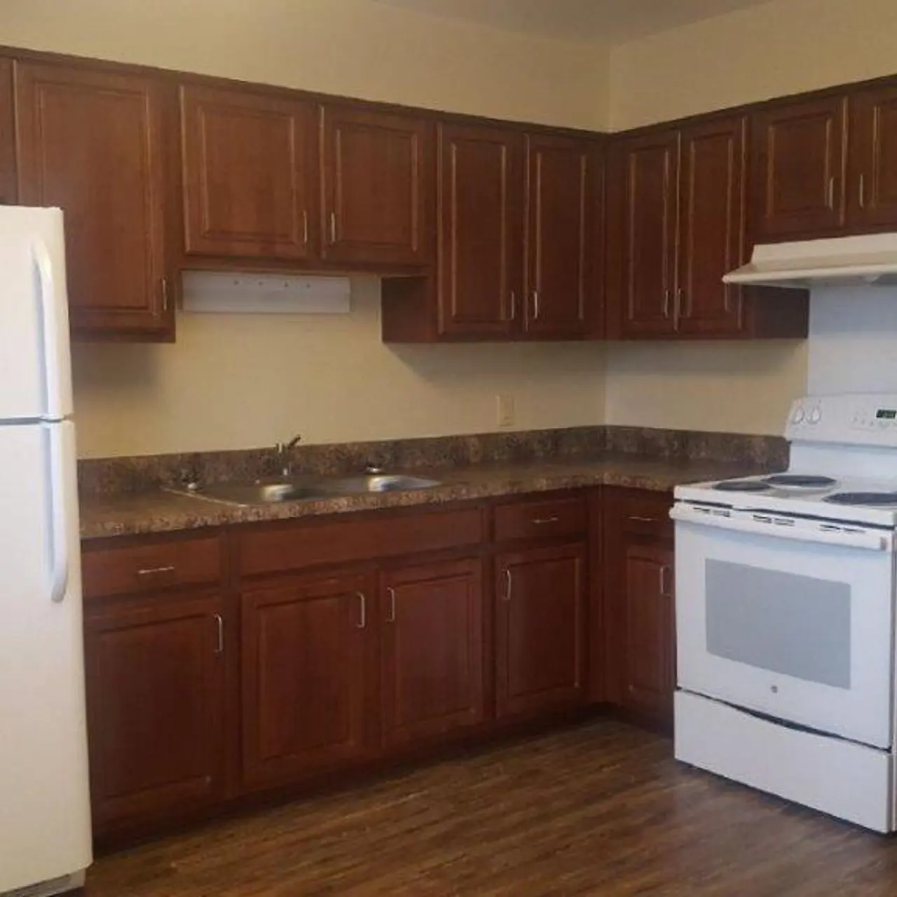 A modern kitchen featuring brown wooden cabinets, a white refrigerator, a white oven, and a sink with a countertop.