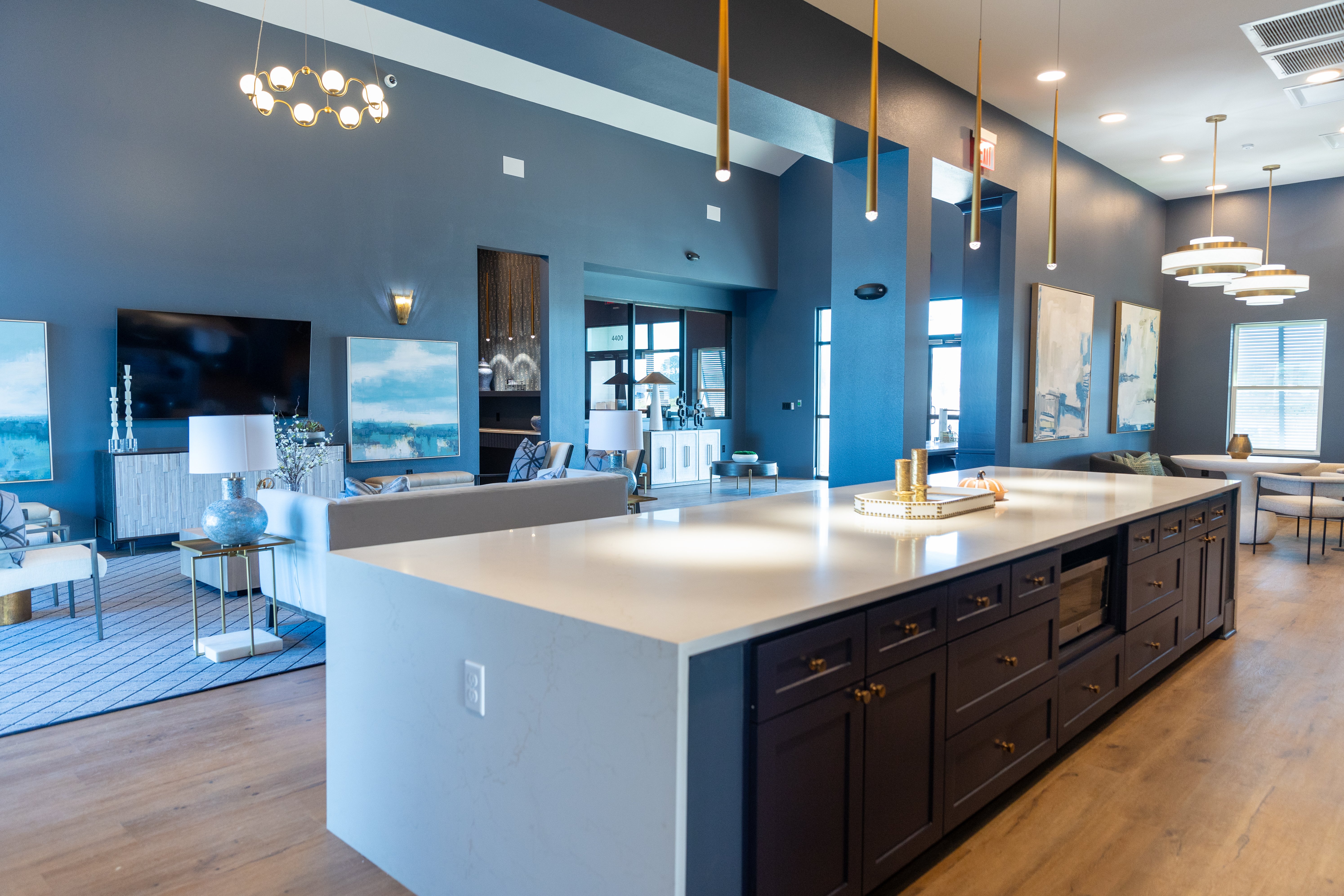 A stylish kitchen with a large island, dark cabinets, and white countertops, leading into a living area with modern furniture and art on the walls.