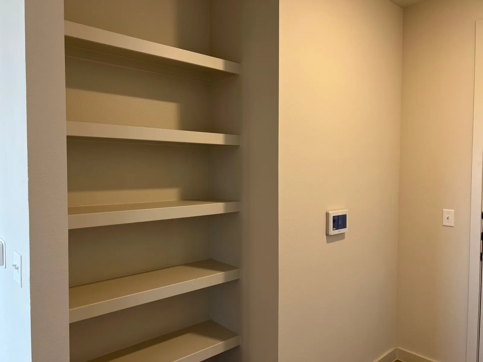 Empty Shelves with Thermostat A section of a wall featuring empty shelves and a thermostat on the side.