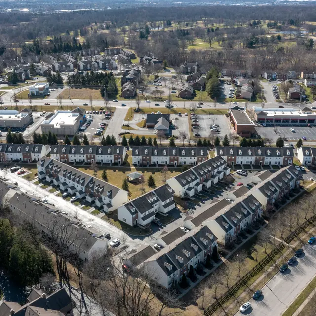 Aerial view of a suburban residential area featuring townhouses, parking, and greenery.
