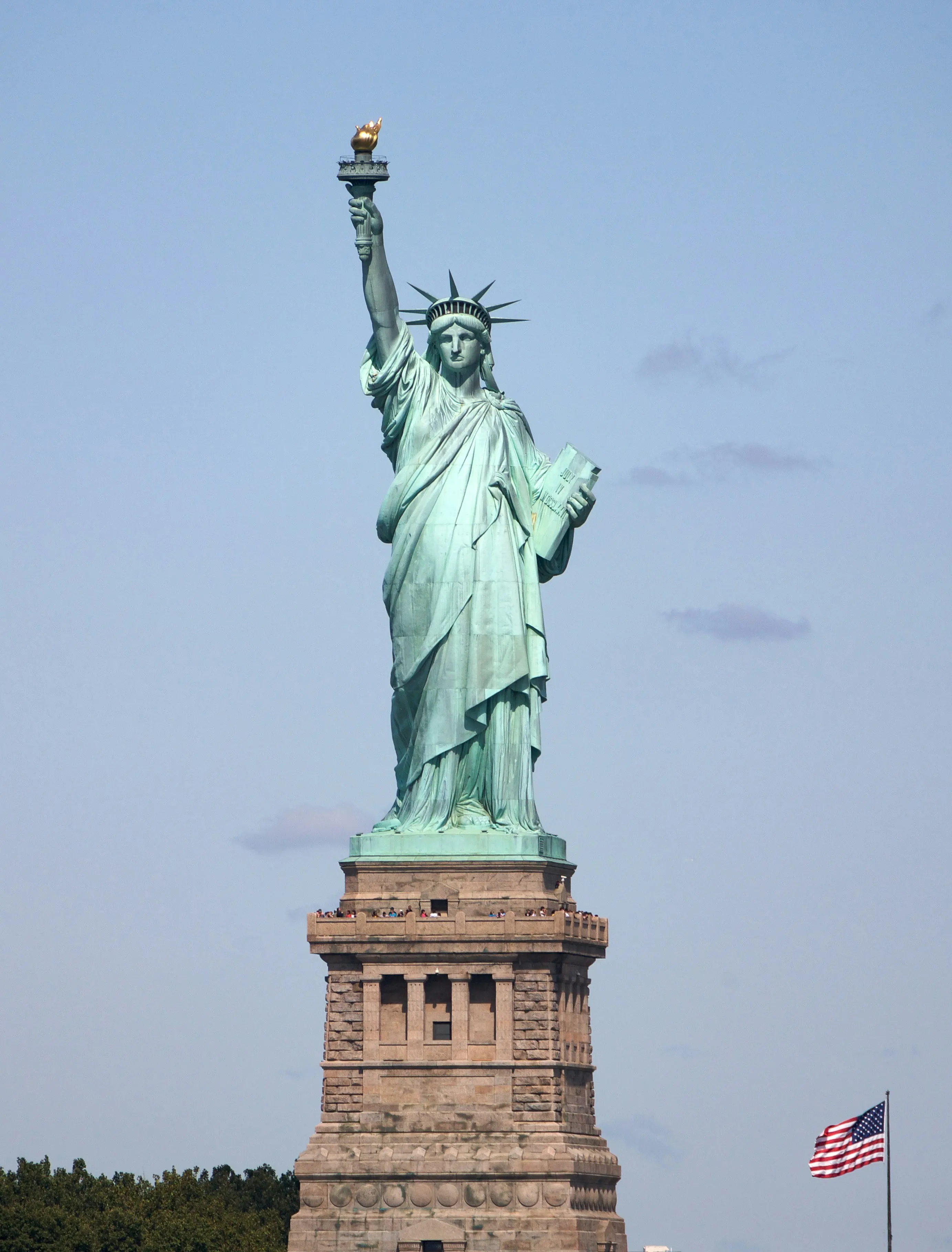 Statue of Liberty standing tall with an American flag in the background on a clear day.