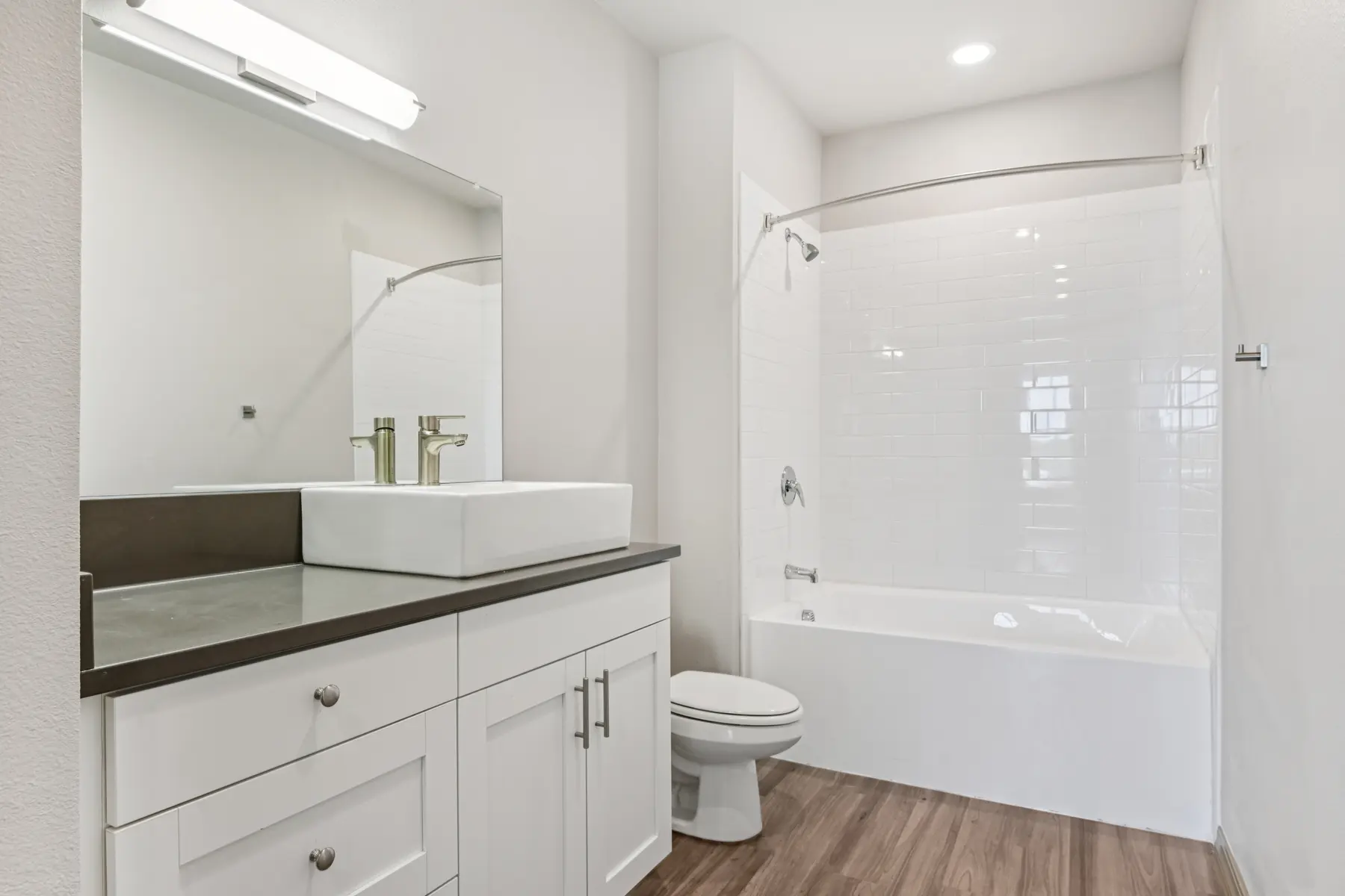 Modern bathroom featuring a white bathtub, shower, stylish sink vanity, large mirror, and light wood flooring.