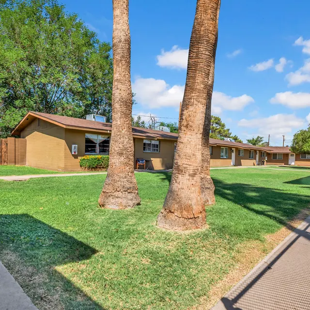 View of an apartment complex with a grassy courtyard, palm trees, and blue skies.