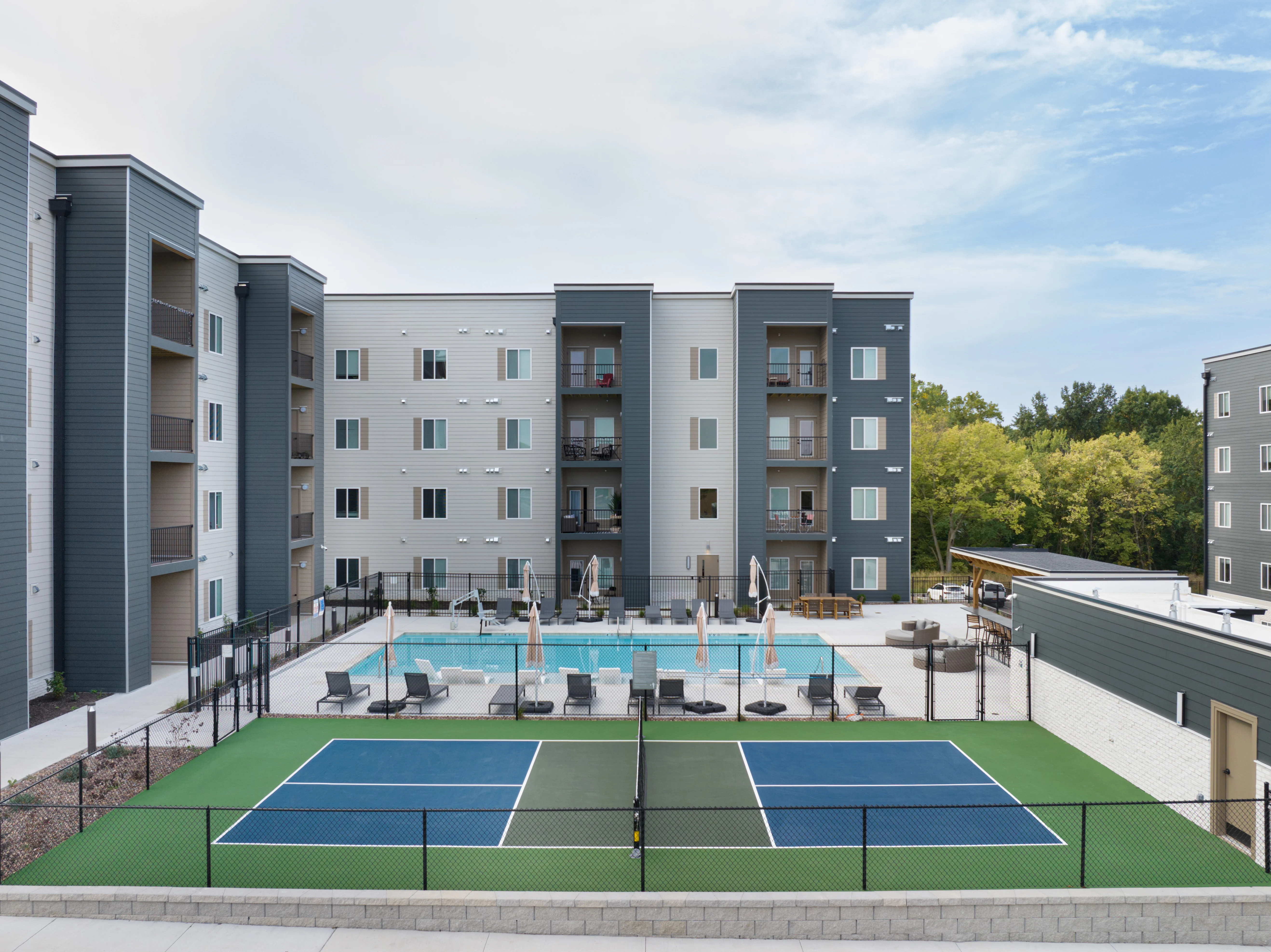 Modern Apartment Community with Pool and Tennis Court View of a modern apartment complex featuring a swimming pool and tennis court.
