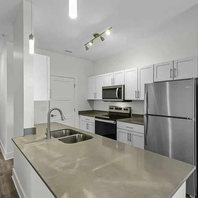 A modern kitchen featuring a large island with sink, stainless steel appliances, and white cabinetry against a light-colored wall.
