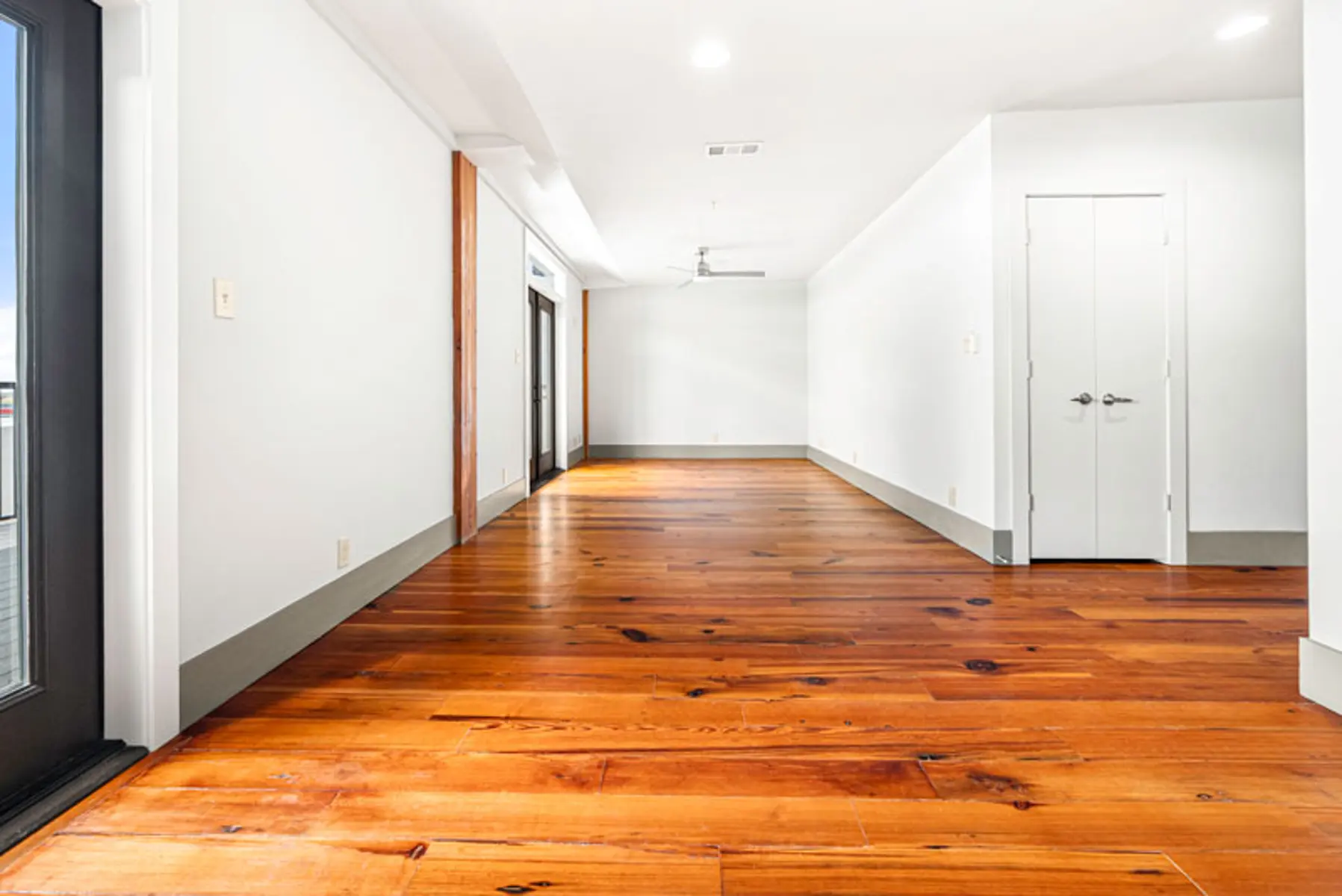 A spacious, modern apartment interior featuring polished wooden floors and white walls.