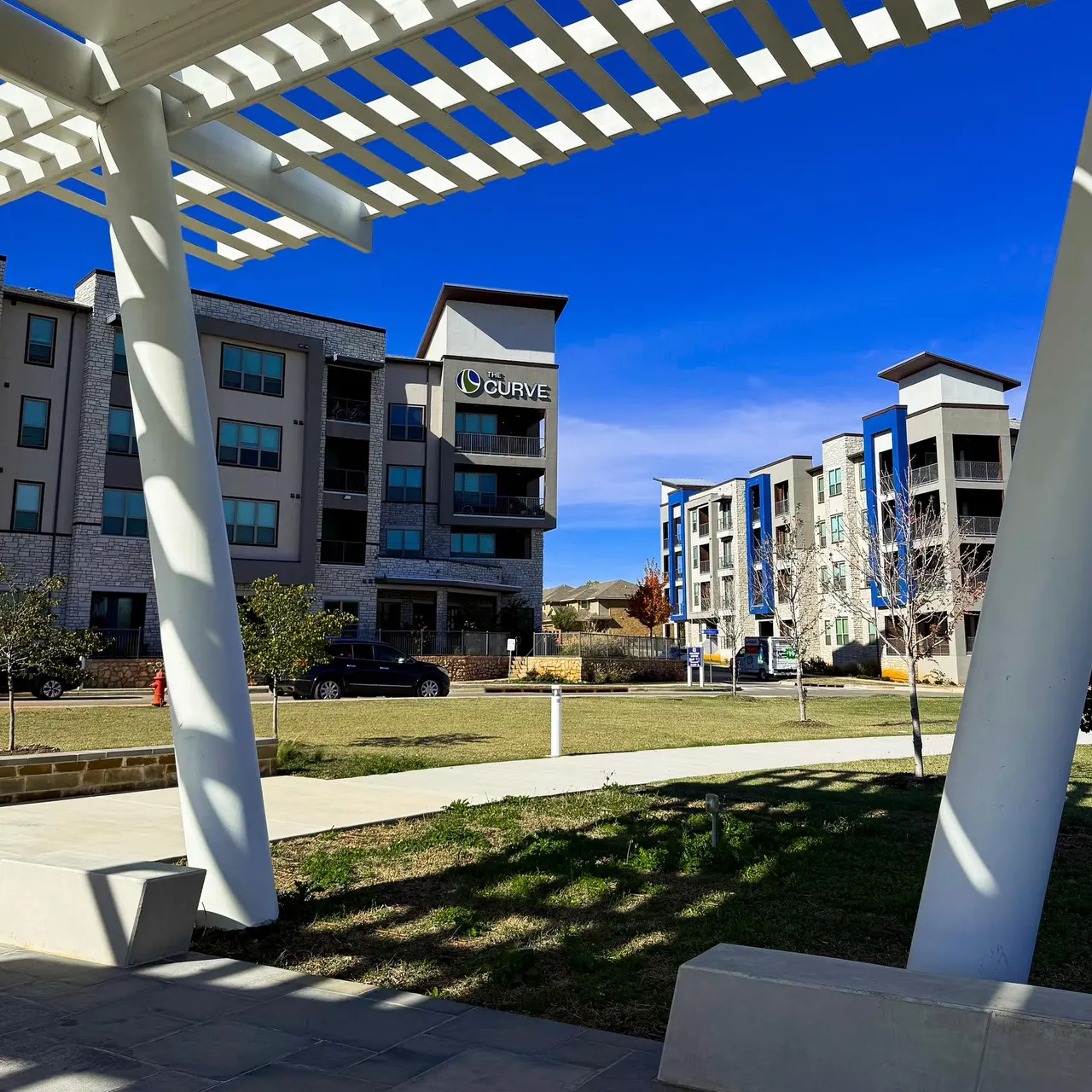 Modern Apartment Complex View of a modern apartment complex surrounded by greenery under a clear blue sky.
