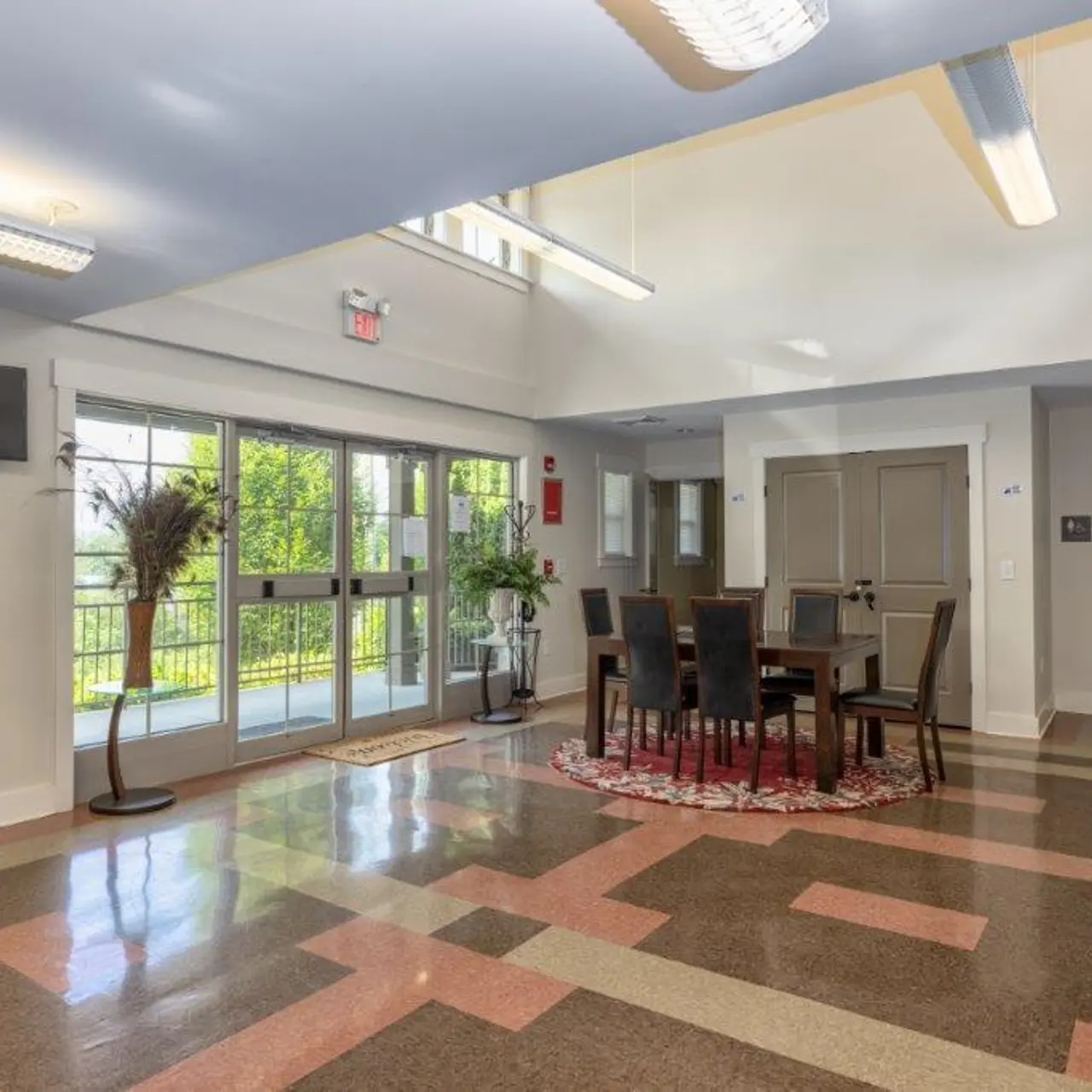 Interior view of a community center showcasing a dining area with a table and chairs, large windows, and polished flooring.