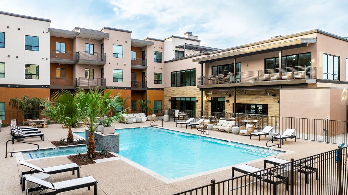 Modern Apartment Complex Pool Area View of a modern apartment complex with a swimming pool surrounded by lounge chairs and palm trees.