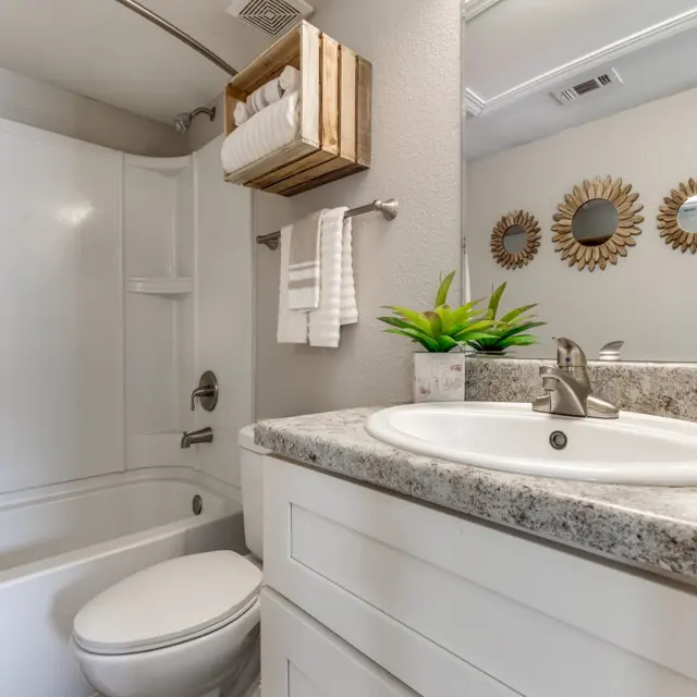A modern bathroom featuring a white tub and shower, a granite countertop sink, and decorative mirrors.