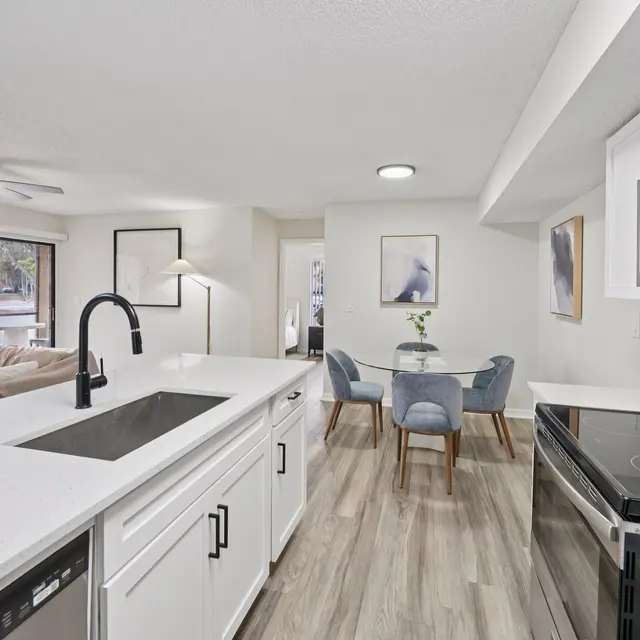 A modern kitchen with white cabinets, a large island with a sink, stainless steel appliances, and a spacious dining area with a table and chairs.
